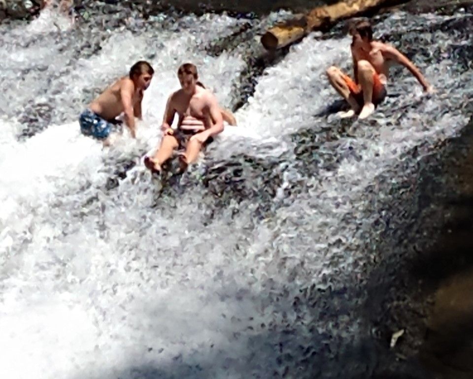 Three people sitting and sliding down a fast-flowing waterfall over dark rocks