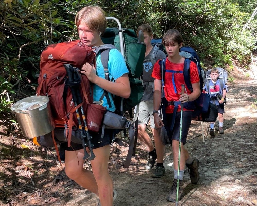 Hikers with backpacks and trekking poles walking along a wooded trail