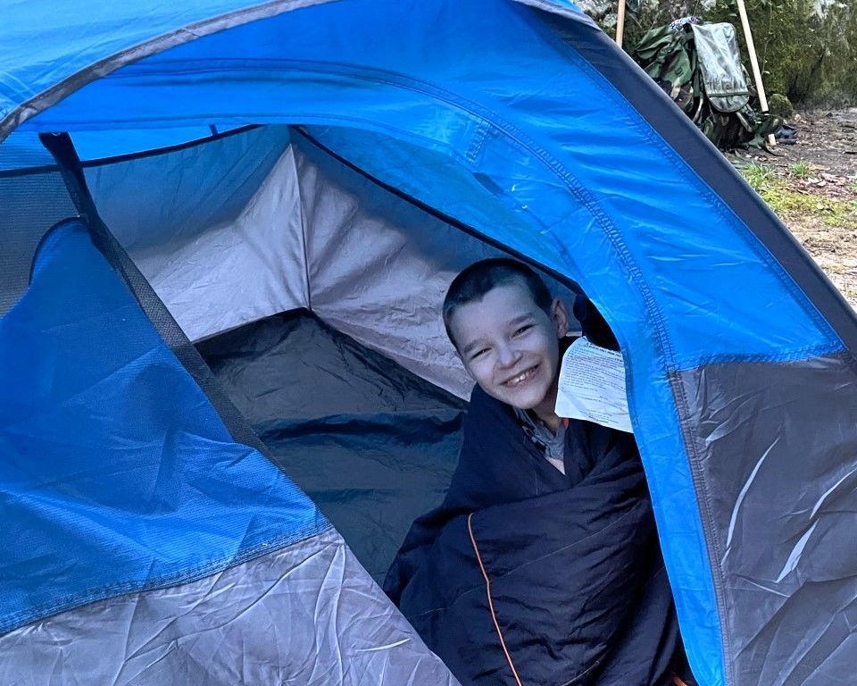 Child smiling inside a blue and gray tent outdoors