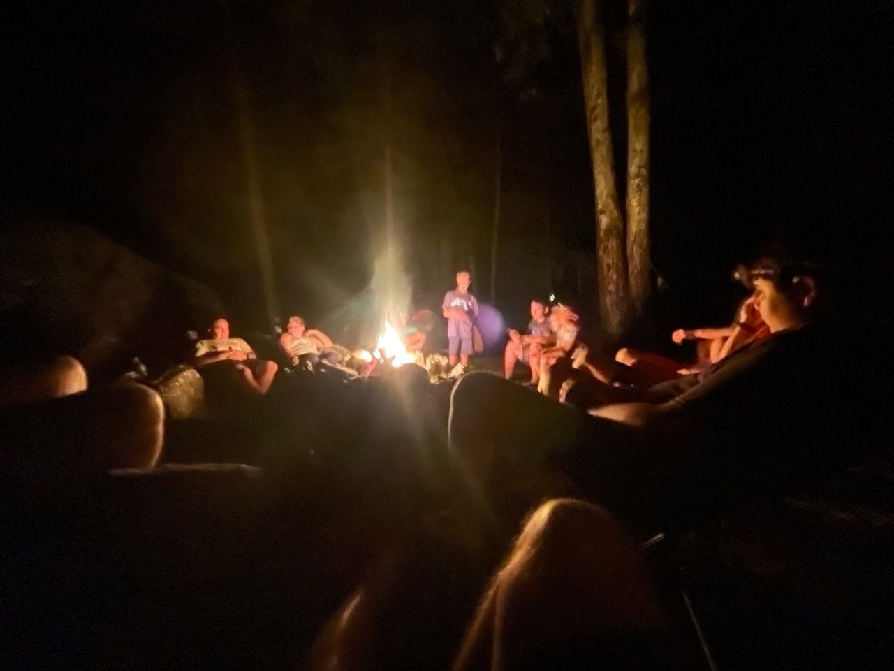 People gathered around a bright campfire at night in a wooded clearing
