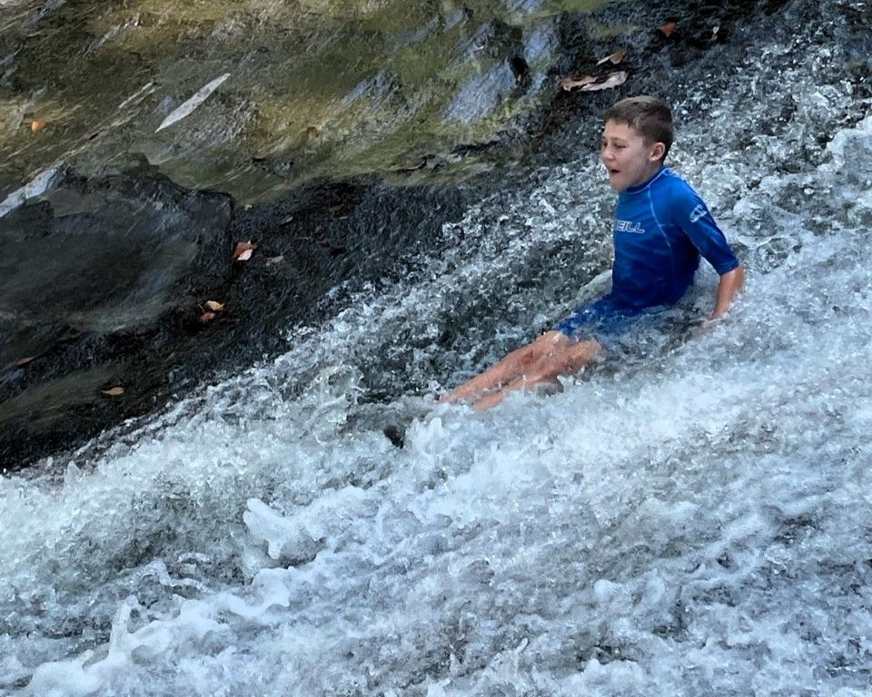 Person in a blue shirt sliding through rushing whitewater on a rocky stream.