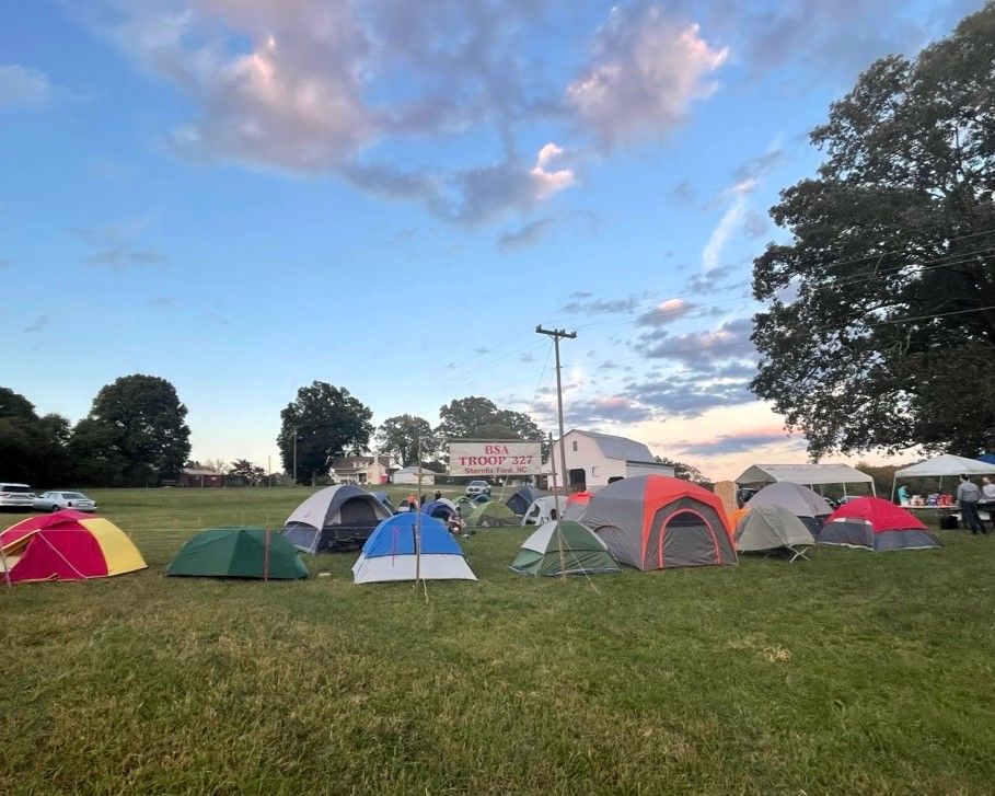 Colorful tents pitched on a grassy field at dusk with a cloudy sky and trees nearby