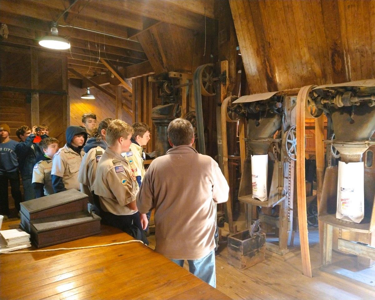 Group of people touring a rustic wooden interior, looking at machinery and exhibits near a lit display