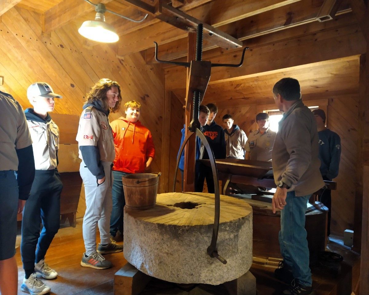 People gathered around a large circular millstone in a wooden workshop, examining the equipment.