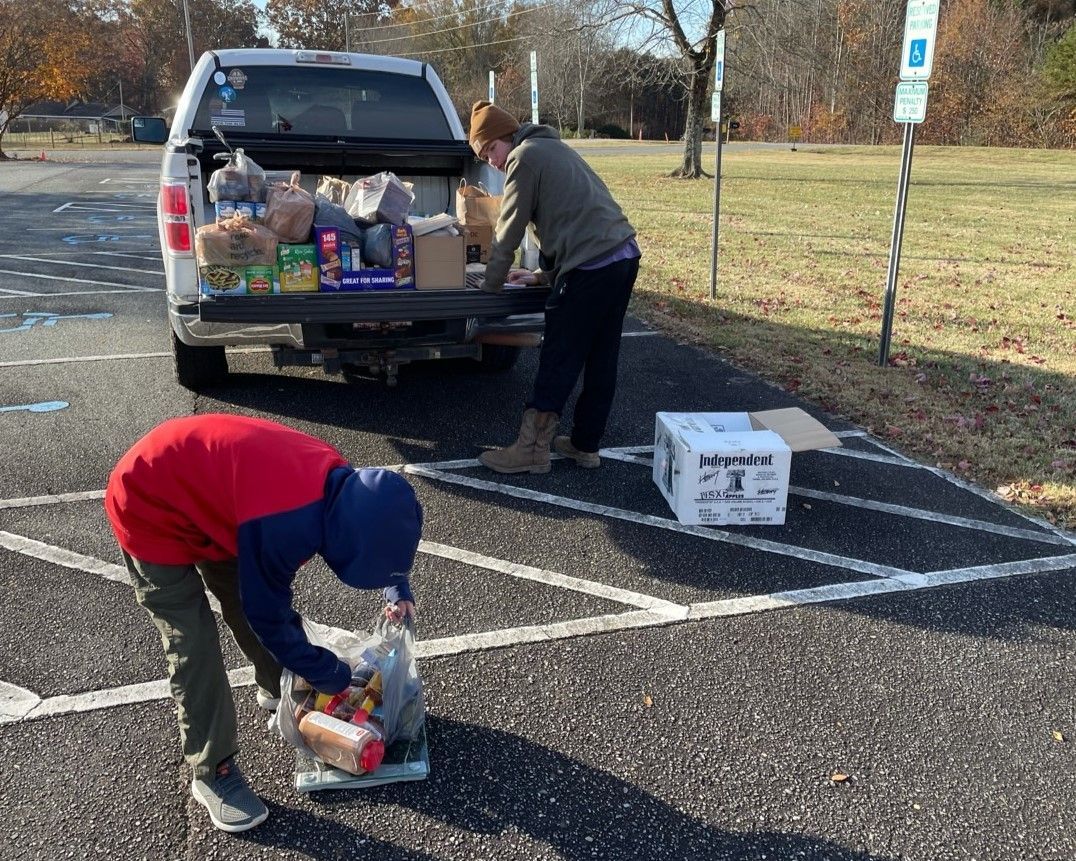 People unloading food boxes from the back of a pickup truck in a parking lot