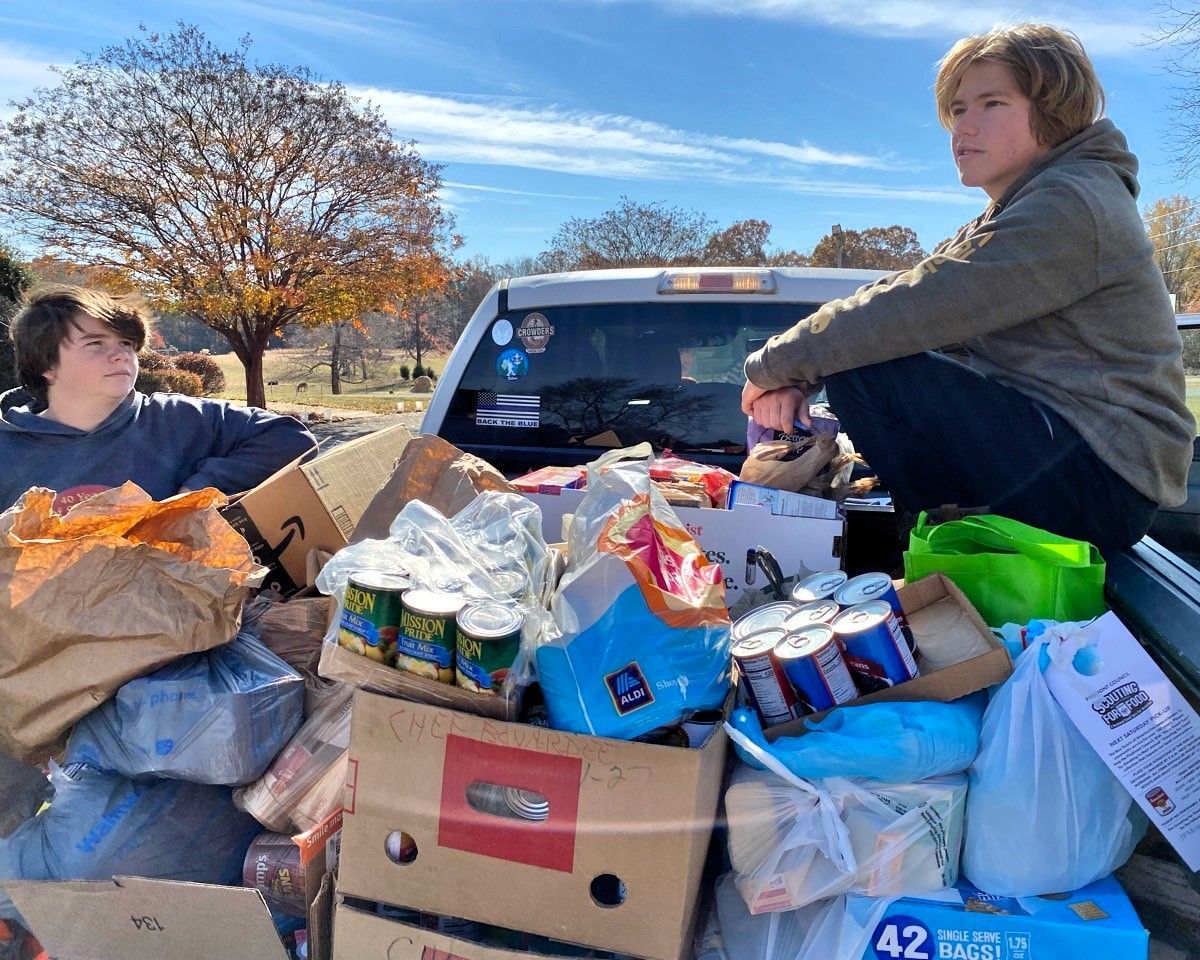 People loading a truck bed with boxes, bags, and supplies outdoors on a sunny day