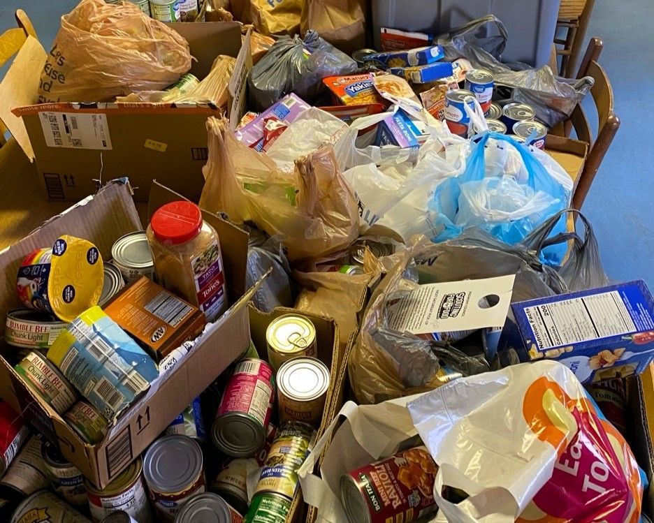 Overflowing pile of food and household items in bags, cans, and boxes on a table