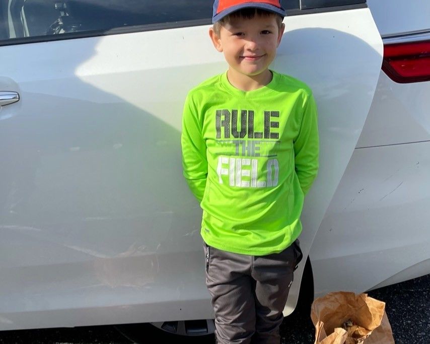 Smiling child in neon green shirt and cap stands by a white car