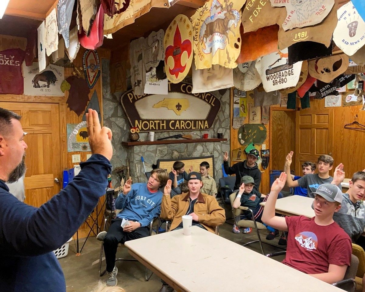 Group raising hands in a rustic room with a “North Carolina” sign overhead.