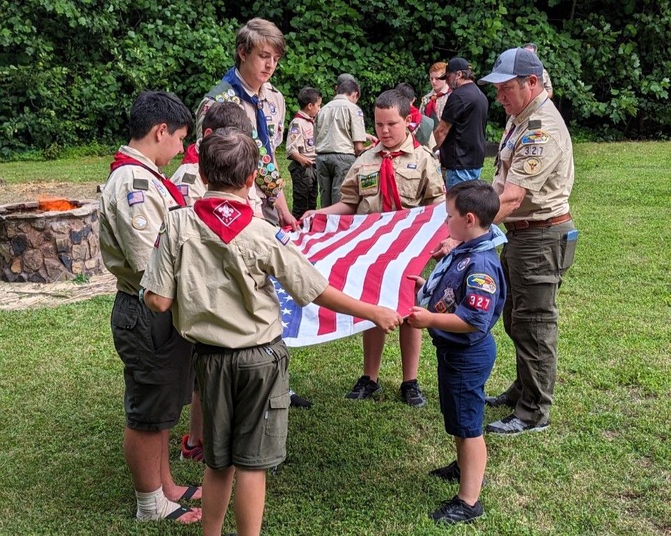 Cub Scouts holding and folding a large American flag during an outdoor ceremony