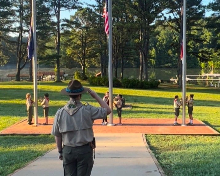 A man in a hat is saluting a flag in a park