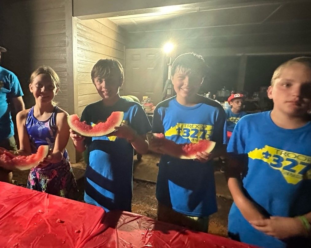 A group of children are standing around a table eating watermelon.