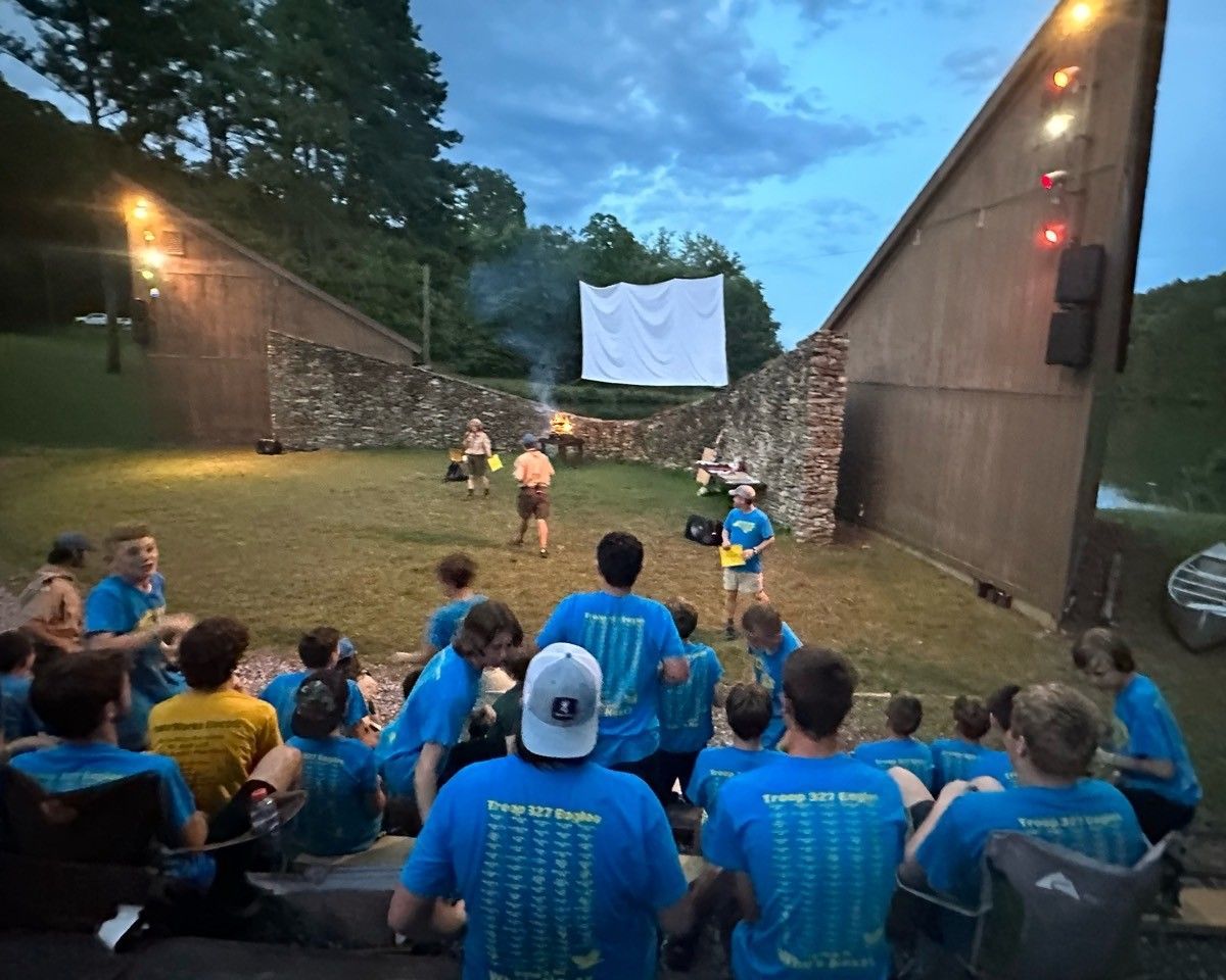 A group of people in blue shirts are sitting in front of a large screen.