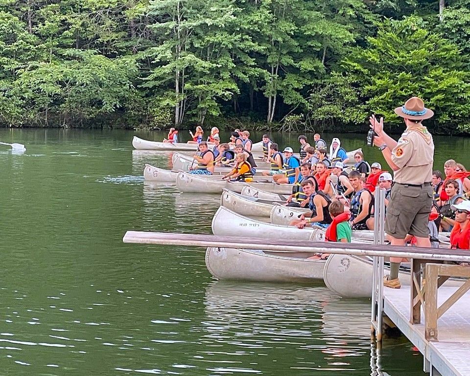 A man is taking a picture of a group of people in canoes on a lake.