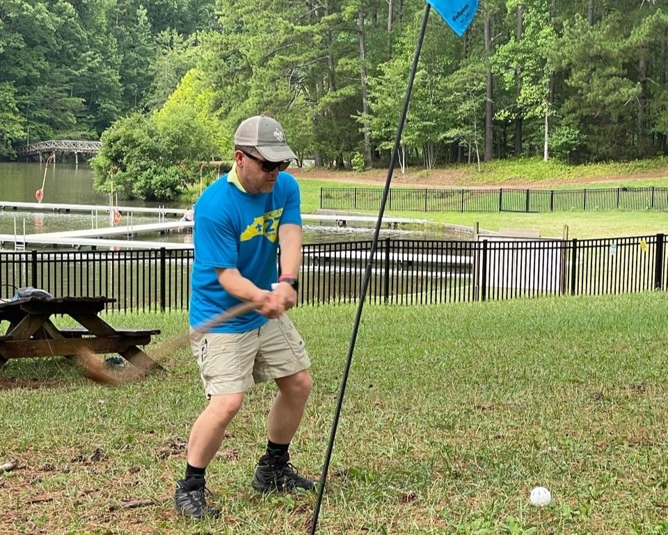 A man in a blue shirt is standing in the grass holding a golf club.