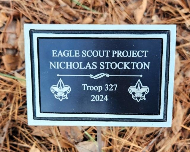 Plaque reading “Eagle Scout Project Nicholas Stockton,” Troop 327, 2024, on wood mulch