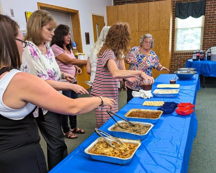 People serving themselves buffet food at a blue-covered table in a wood-paneled room