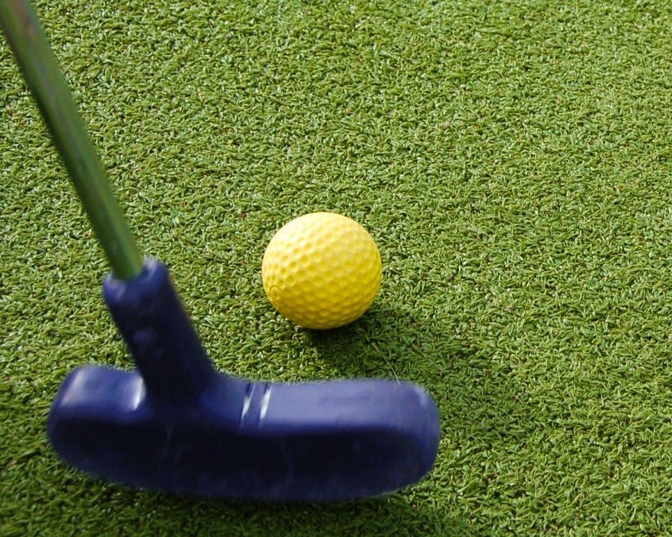 Yellow golf ball beside a blue putter on green artificial turf