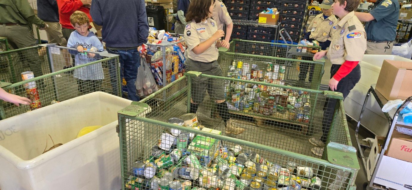 A group of people are standing around a bunch of bins filled with food.