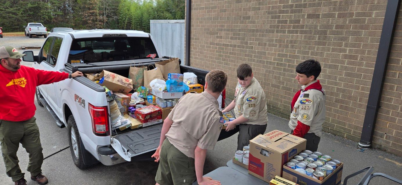 A group of boy scouts are putting food in the back of a truck.