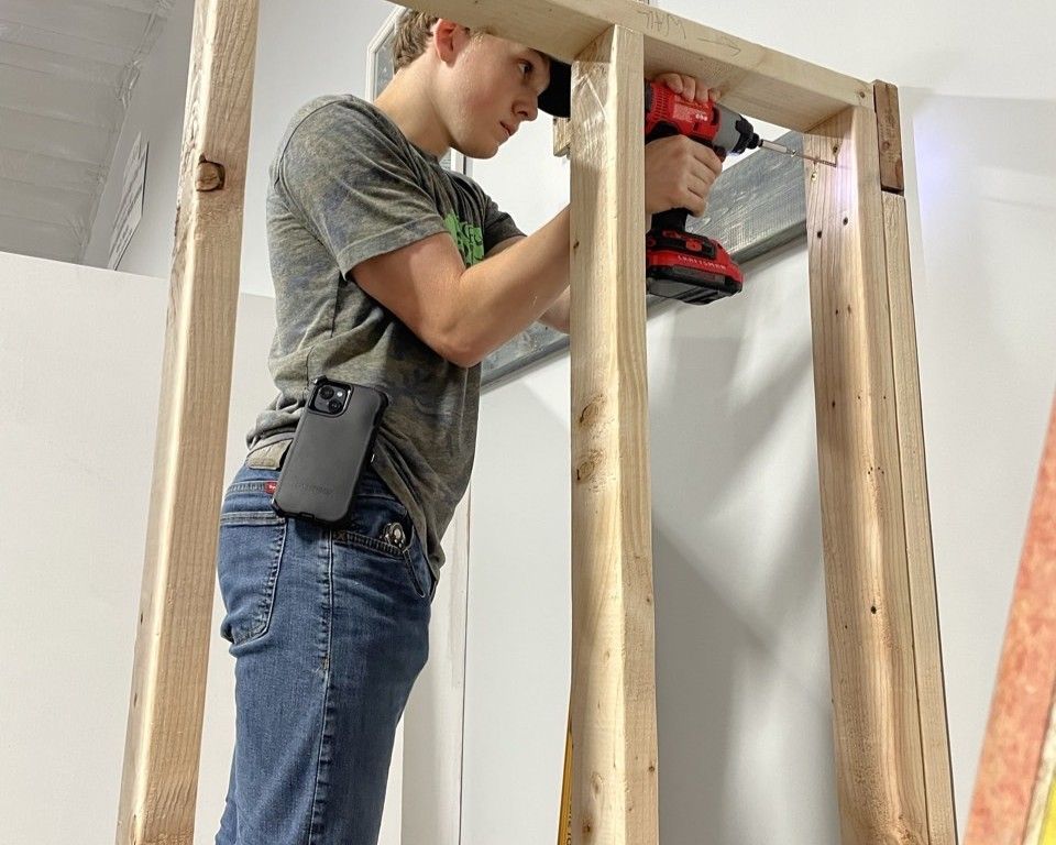 Worker using a red power drill to build a wooden wall frame indoors