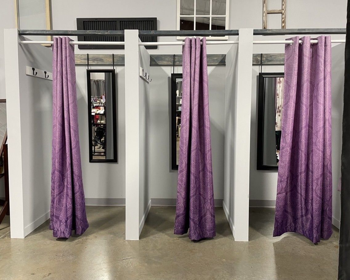 Purple curtains hanging in white changing-room stalls with mirrors and benches in the background