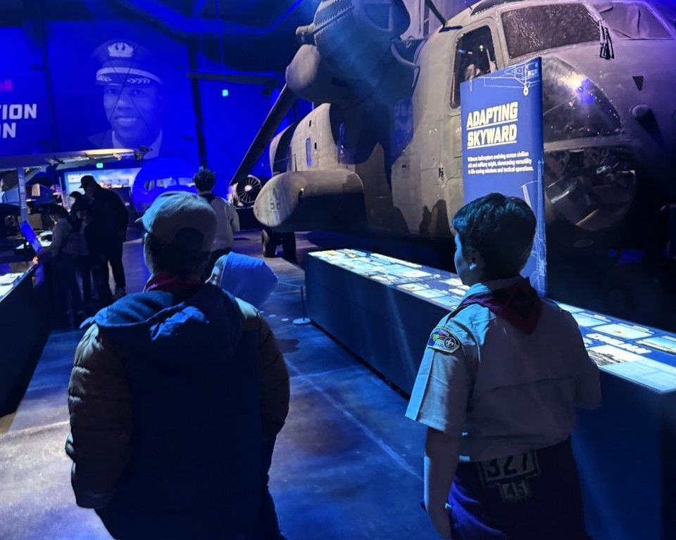 Visitors stand before a blue-lit fighter jet exhibit in a museum.