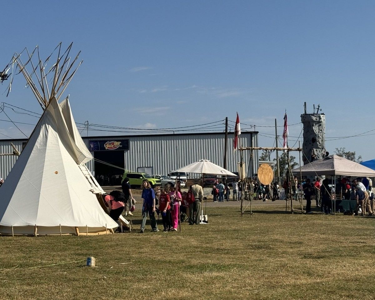 A group of people are standing around a teepee in a field.