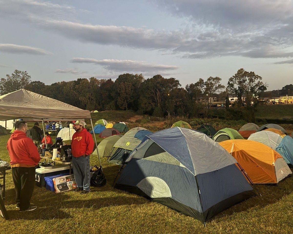 A group of people are standing around tents in a field.