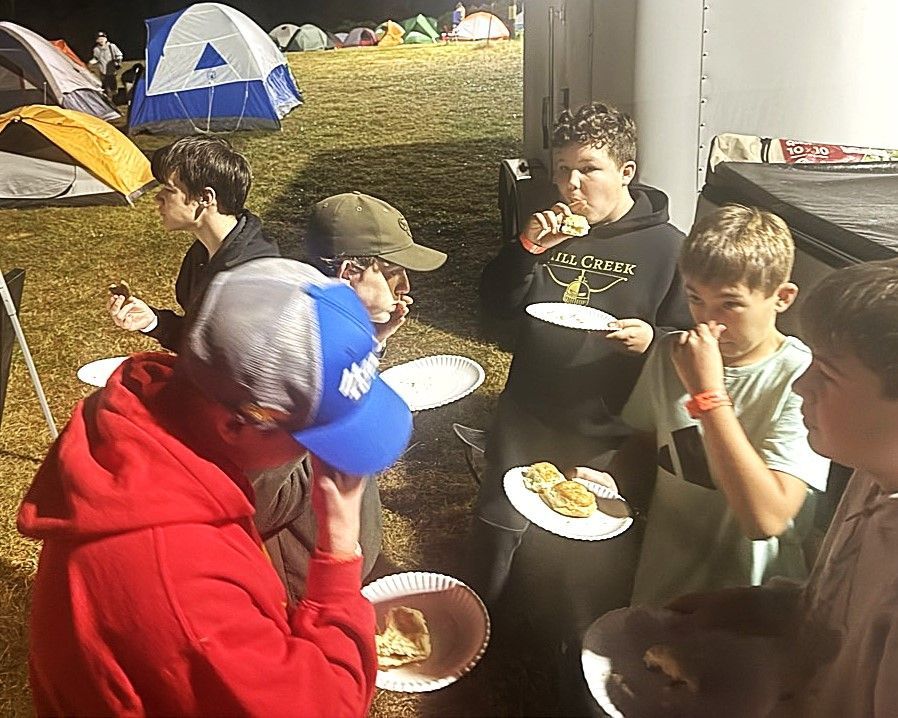 A group of young boys are eating food at a campsite.