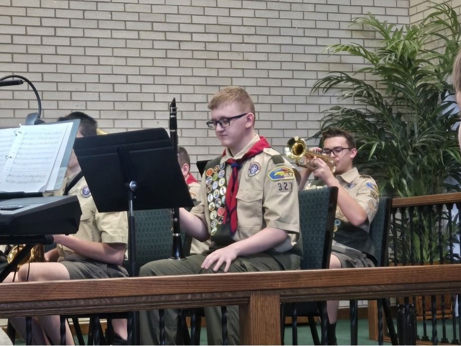 A boy scout is playing a trumpet in an orchestra