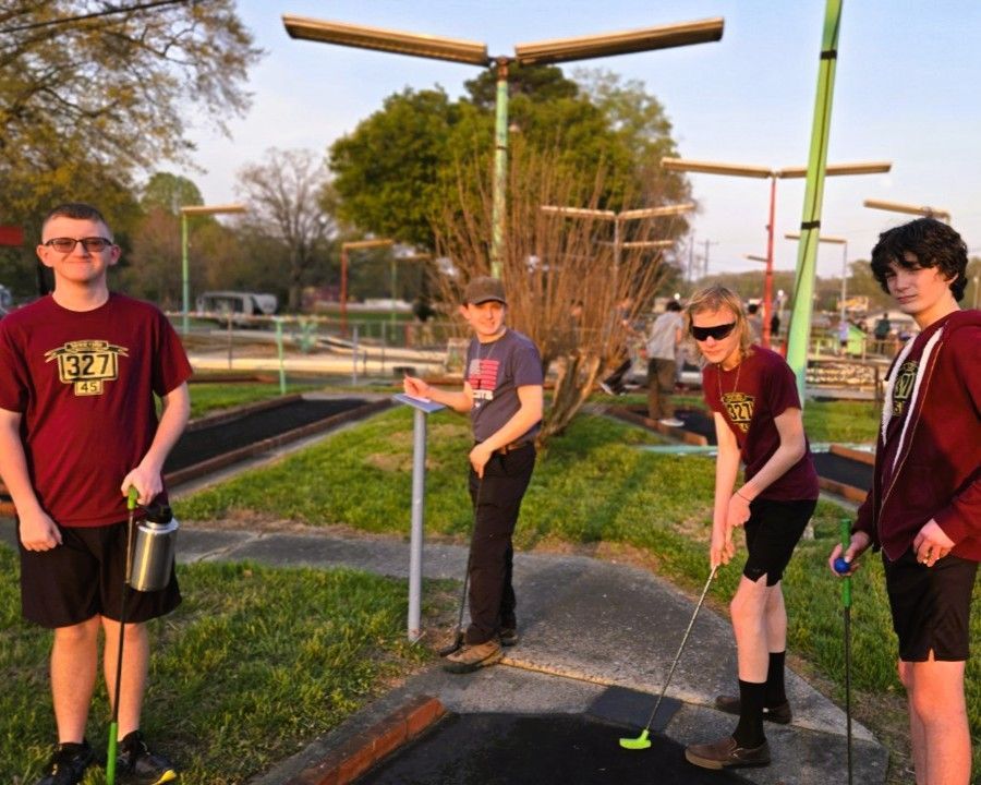 Four teens with long poles standing on a cracked court at sunset near a tennis net