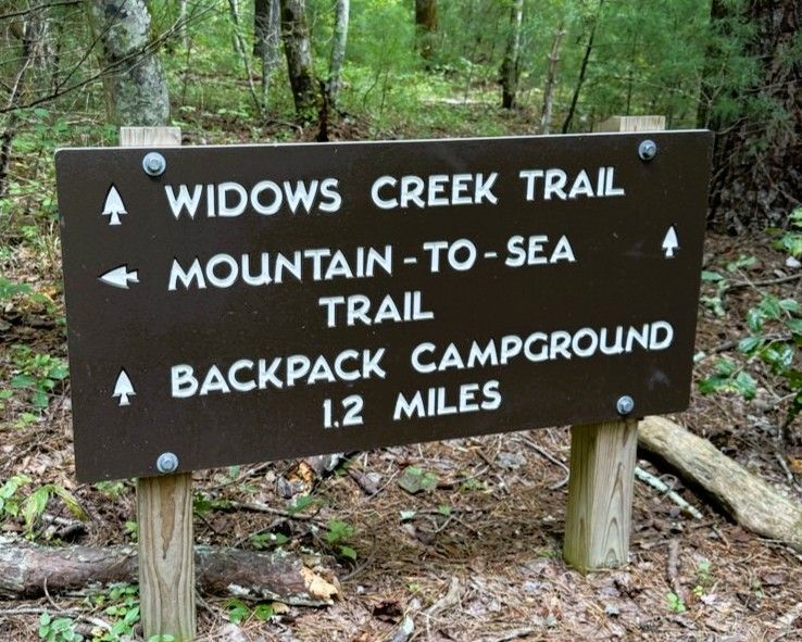 Wooden trail sign in a forest pointing to Widows Creek Trail, Mountain-to-Sea Trail, and Backack Campground