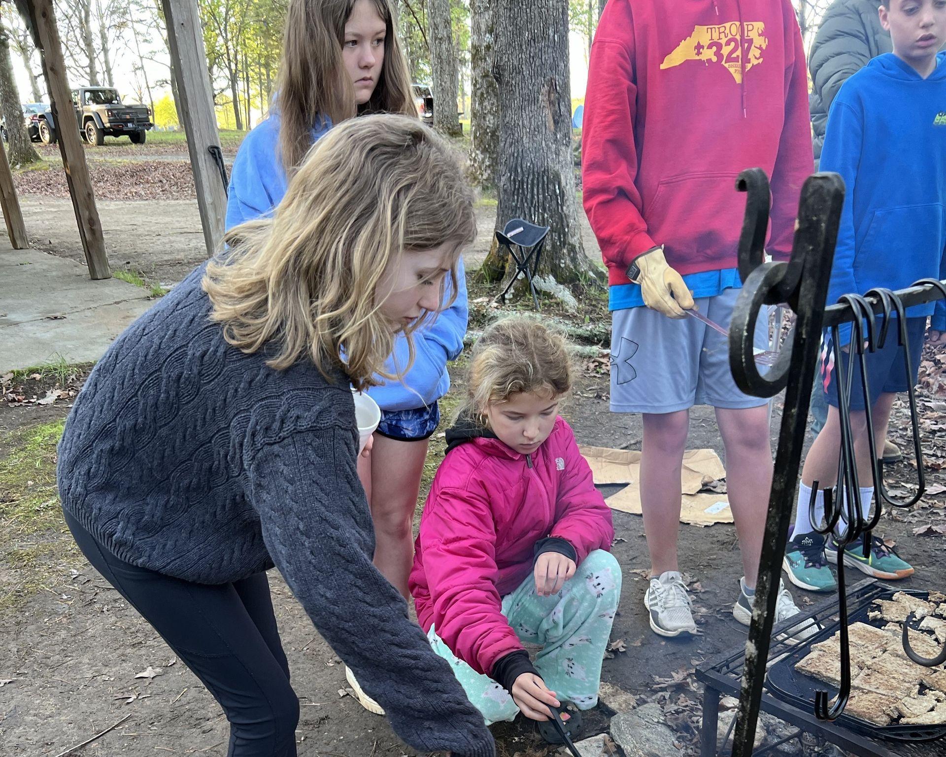 A group of scouts are standing cooking around a fire pit.