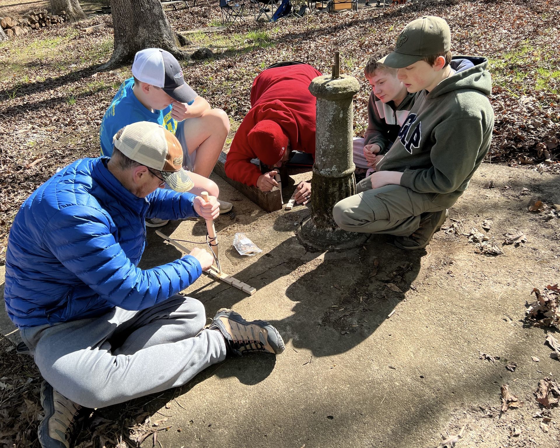 A group of people are sitting on the ground in the woods.