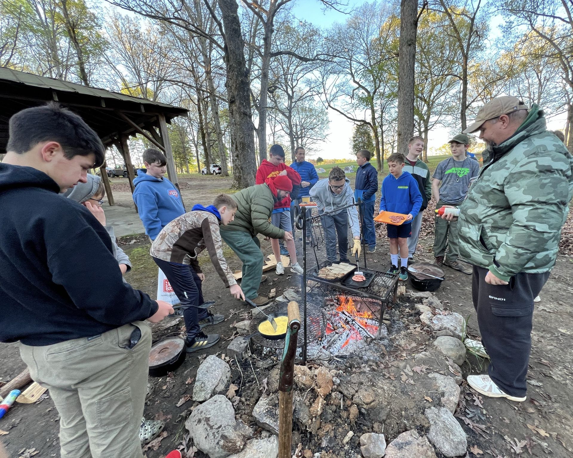 A group of scouts are standing around a campfire cooking food.