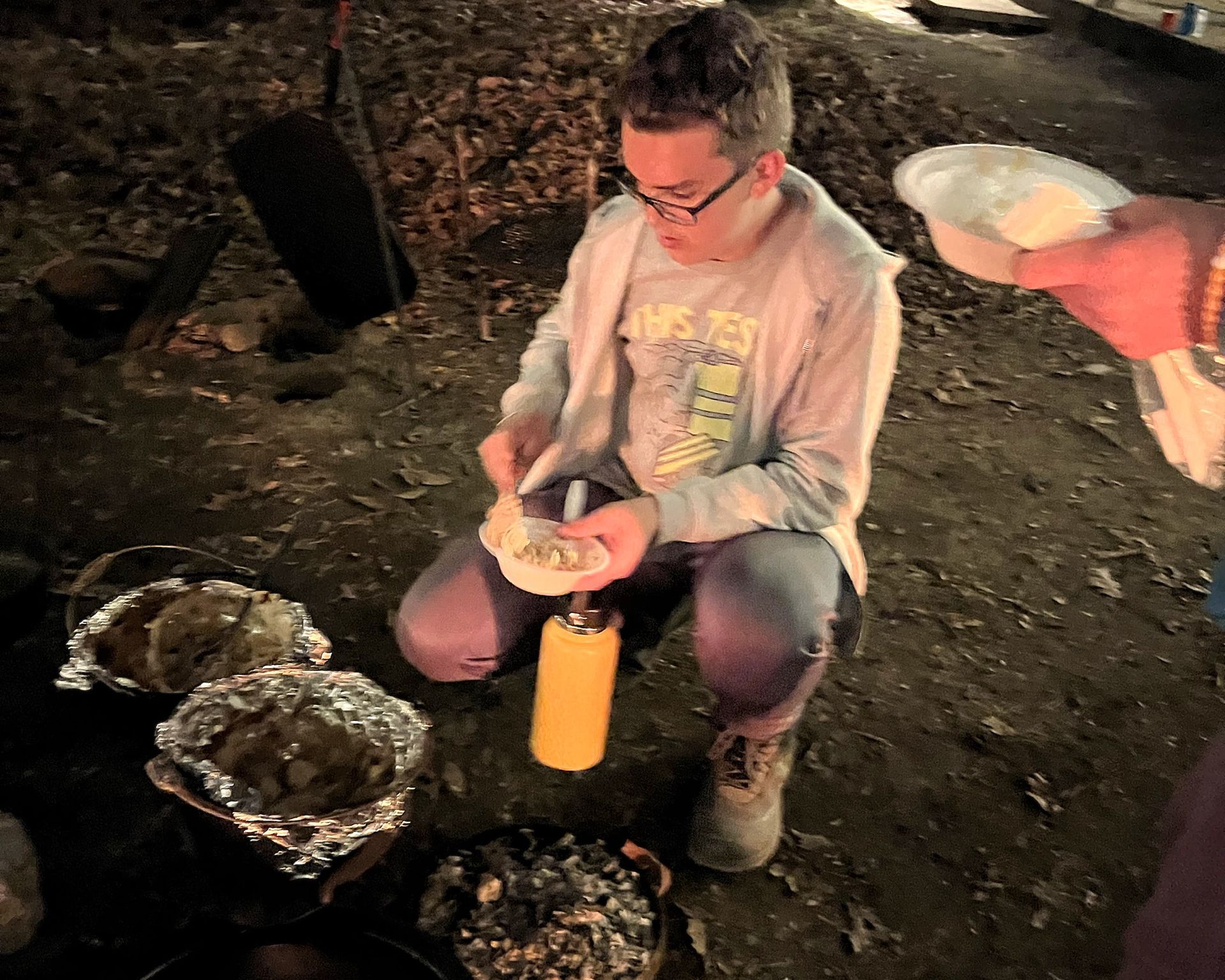 A man is kneeling down with a bottle of mustard in front of him