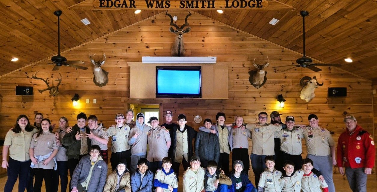 Group of people posing in a rustic lodge hall with wooden walls and a projector screen behind them