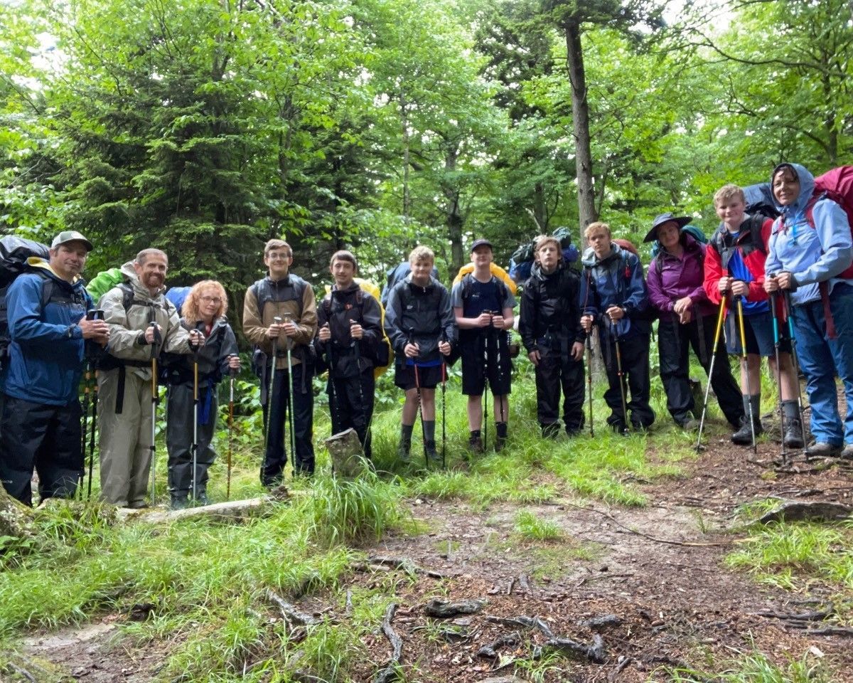 Group of hikers standing on a forest trail, holding trekking poles in a green wooded area.