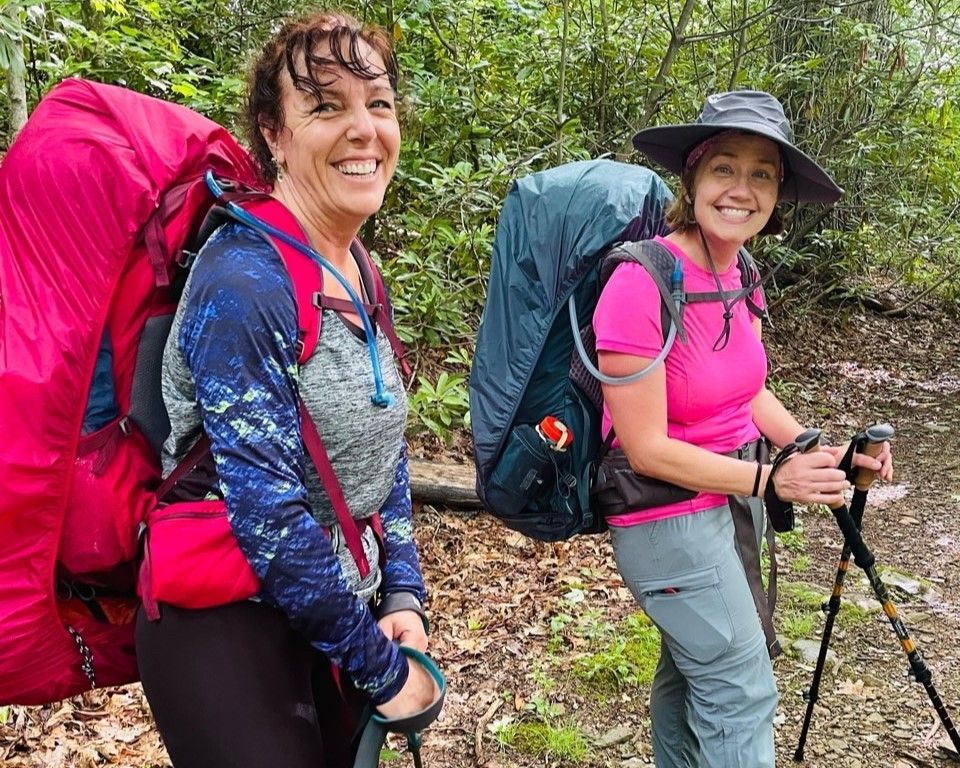 Two hikers with backpacks and trekking poles smiling on a forest trail