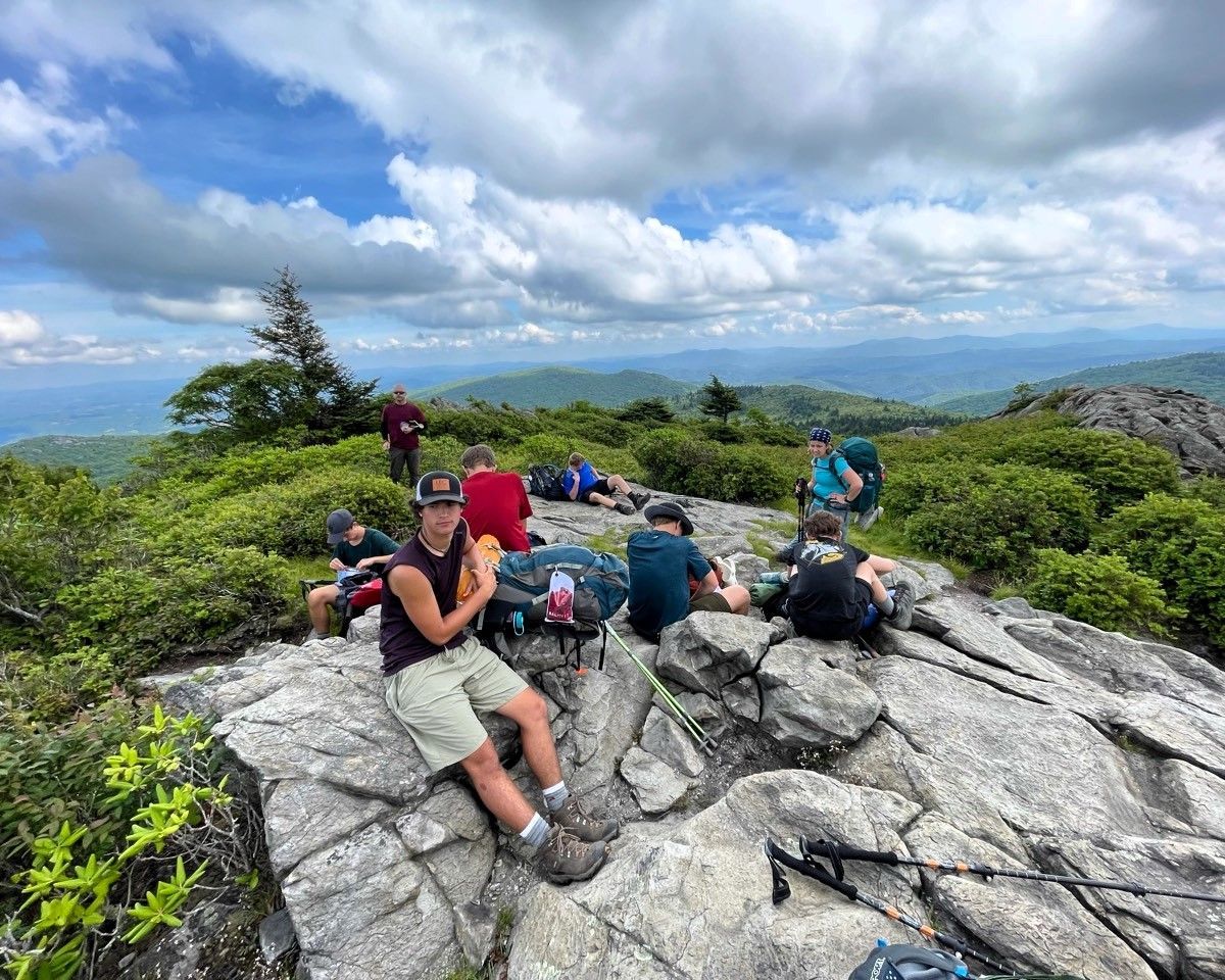 Hikers resting on a rocky summit with cloudy sky and distant mountain views.