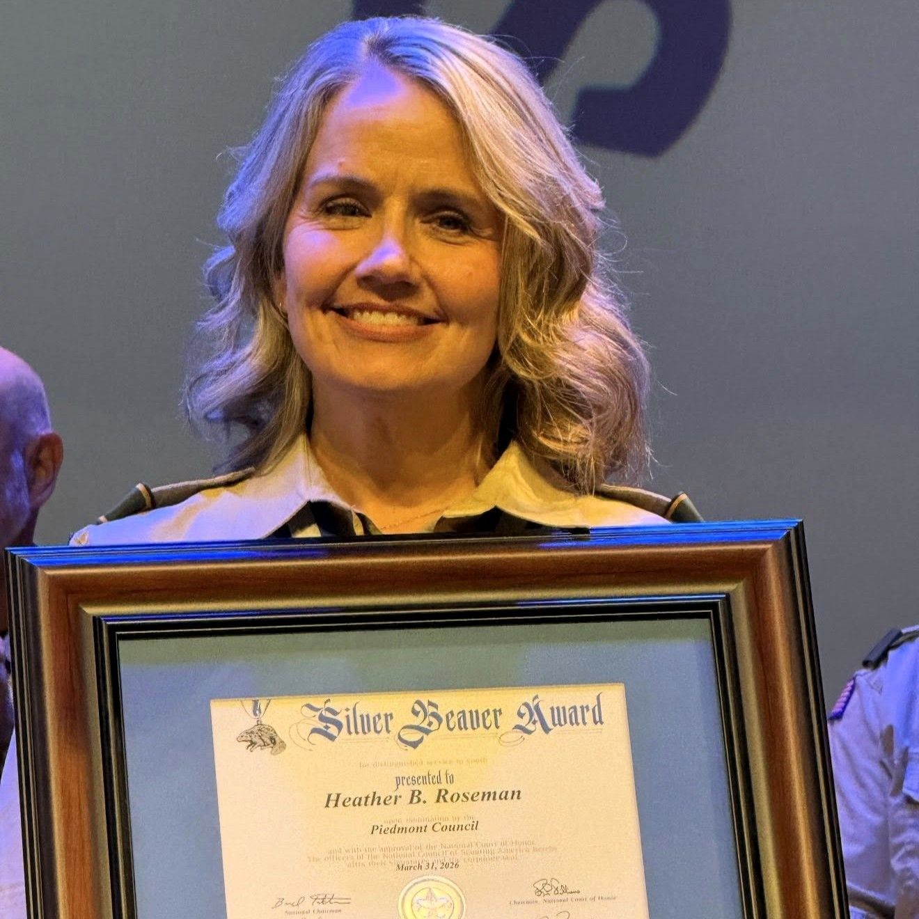 Woman smiling and holding a framed Silver Beaver Award certificate on stage