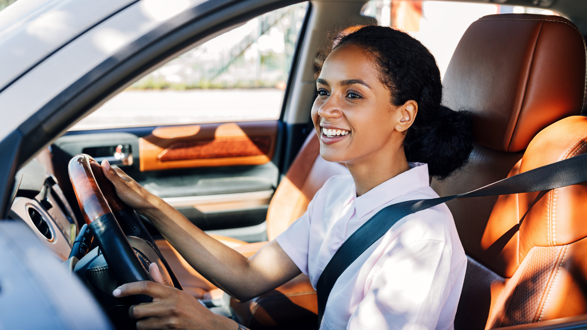 A woman is sitting in the driver 's seat of a car and smiling.