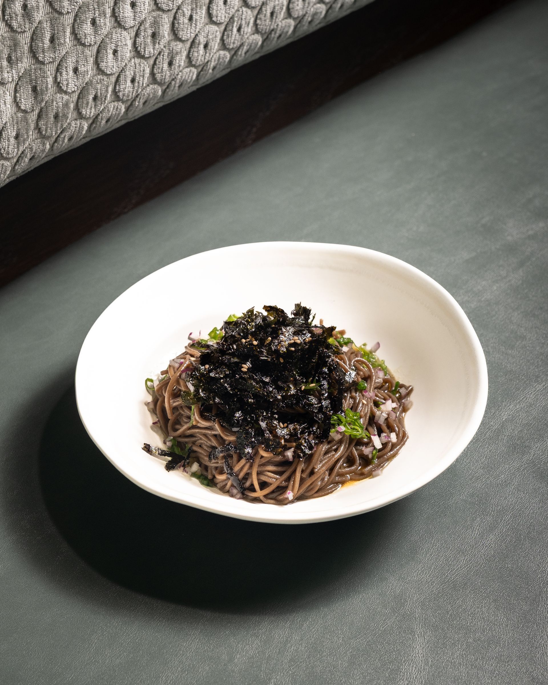 Bowl of noodles with seaweed topping on a green surface.