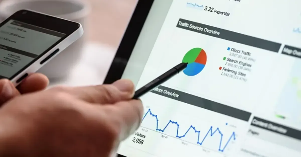Person pointing to a pie chart on a tablet screen, analyzing data with a phone nearby.