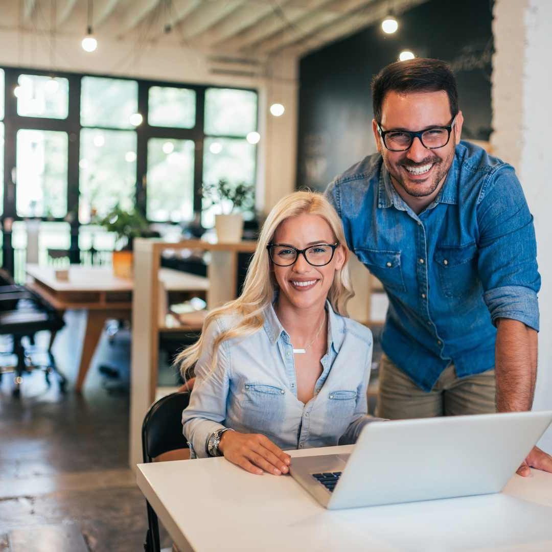 Man and woman smiling over a laptop in a bright office.