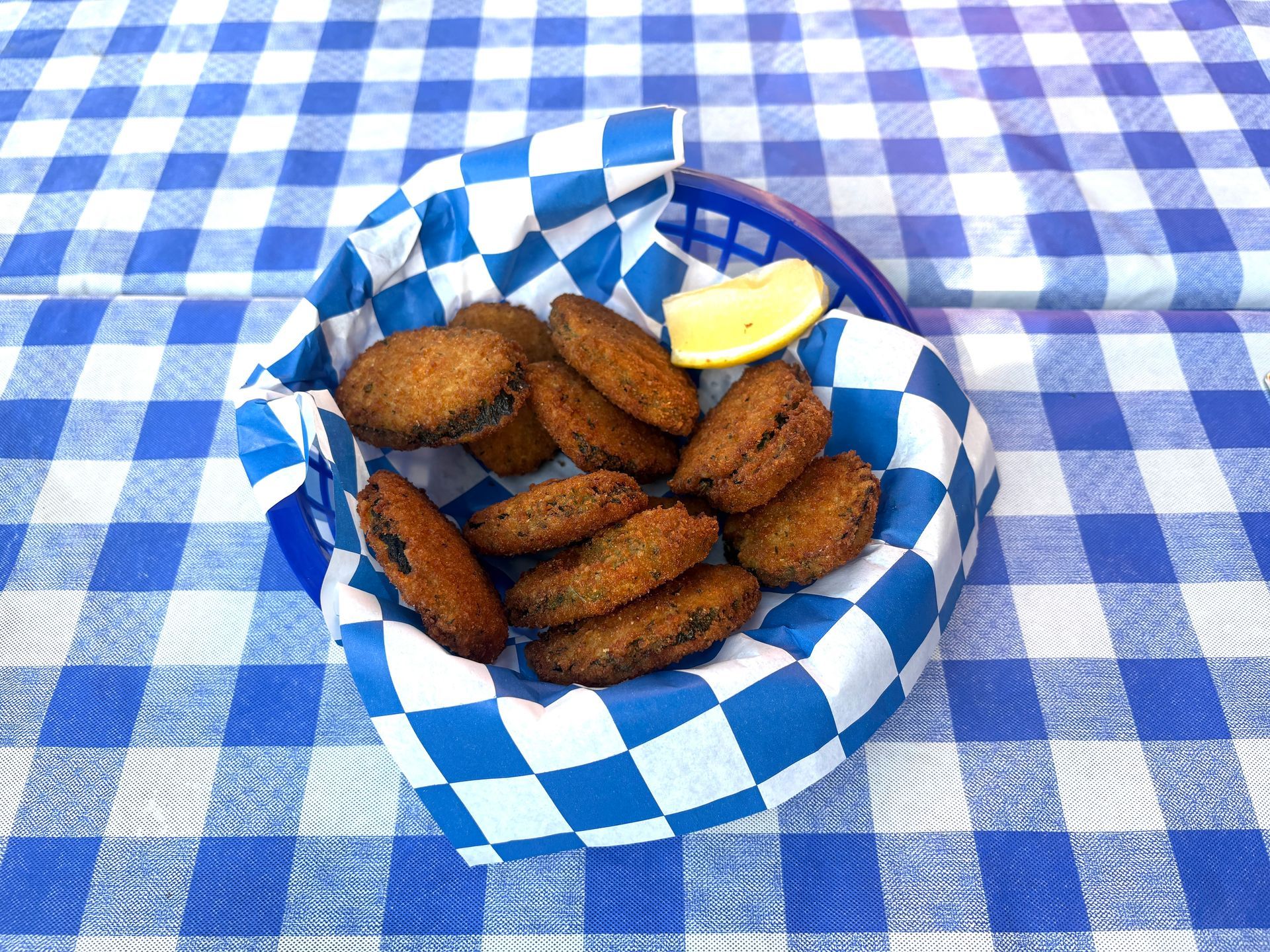 Fried food in a blue basket with a lemon wedge, set on a blue and white checkered tablecloth.