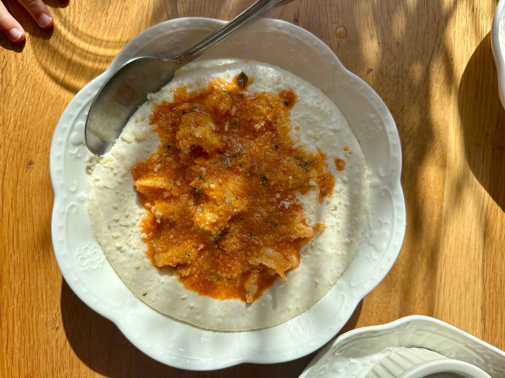 Creamy grits topped with tomato shrimp in a white decorative bowl on a wooden table.