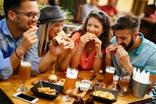 Friends eating burgers and fries at an outdoor restaurant table with beers and a phone.