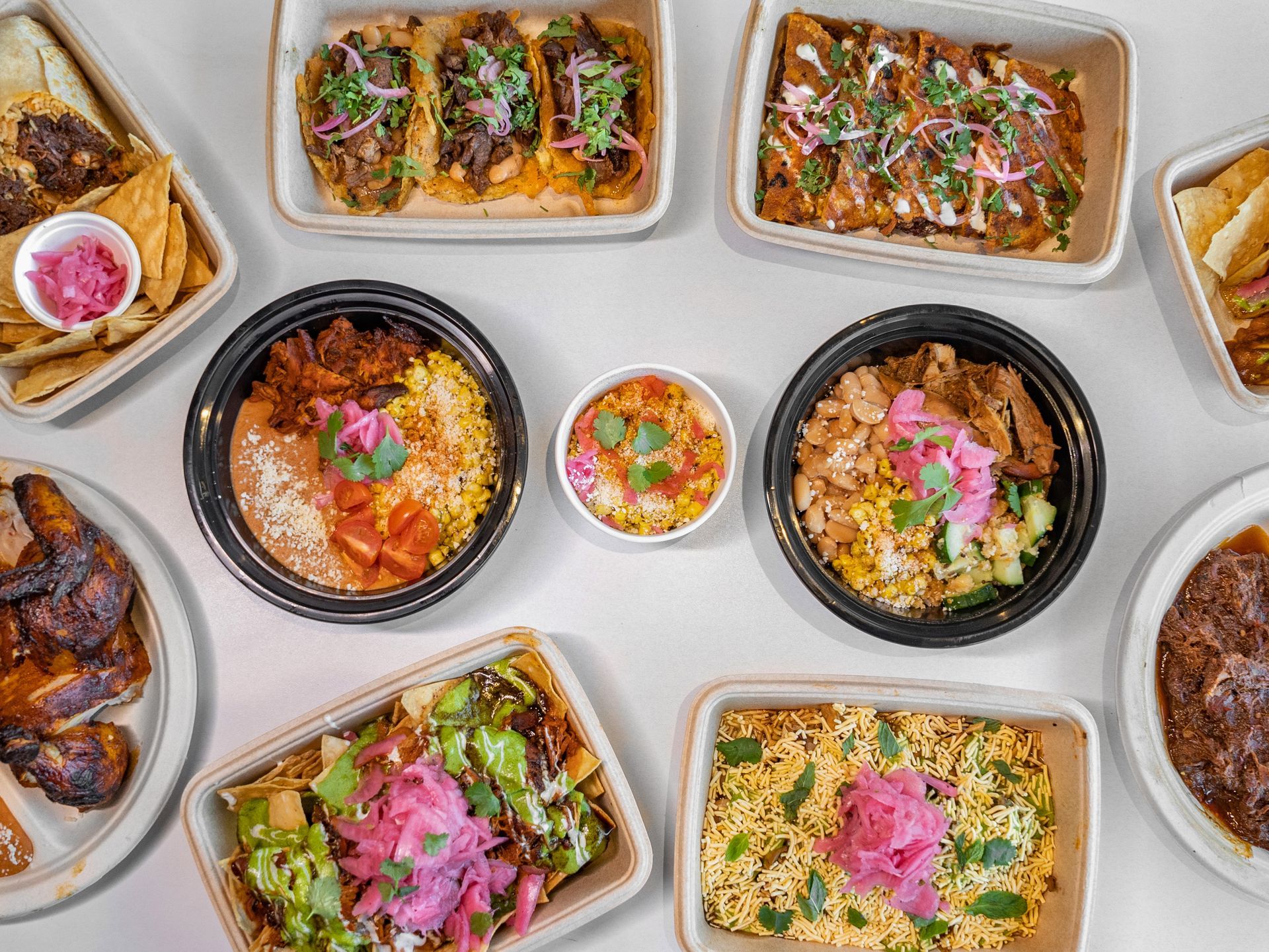 Overhead view of a spread of Mexican food in various containers, including tacos, bowls, and rice dishes.